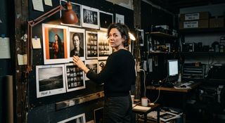 Photographer reviewing contact sheets and prints pinned to the wall of her darkroom studio